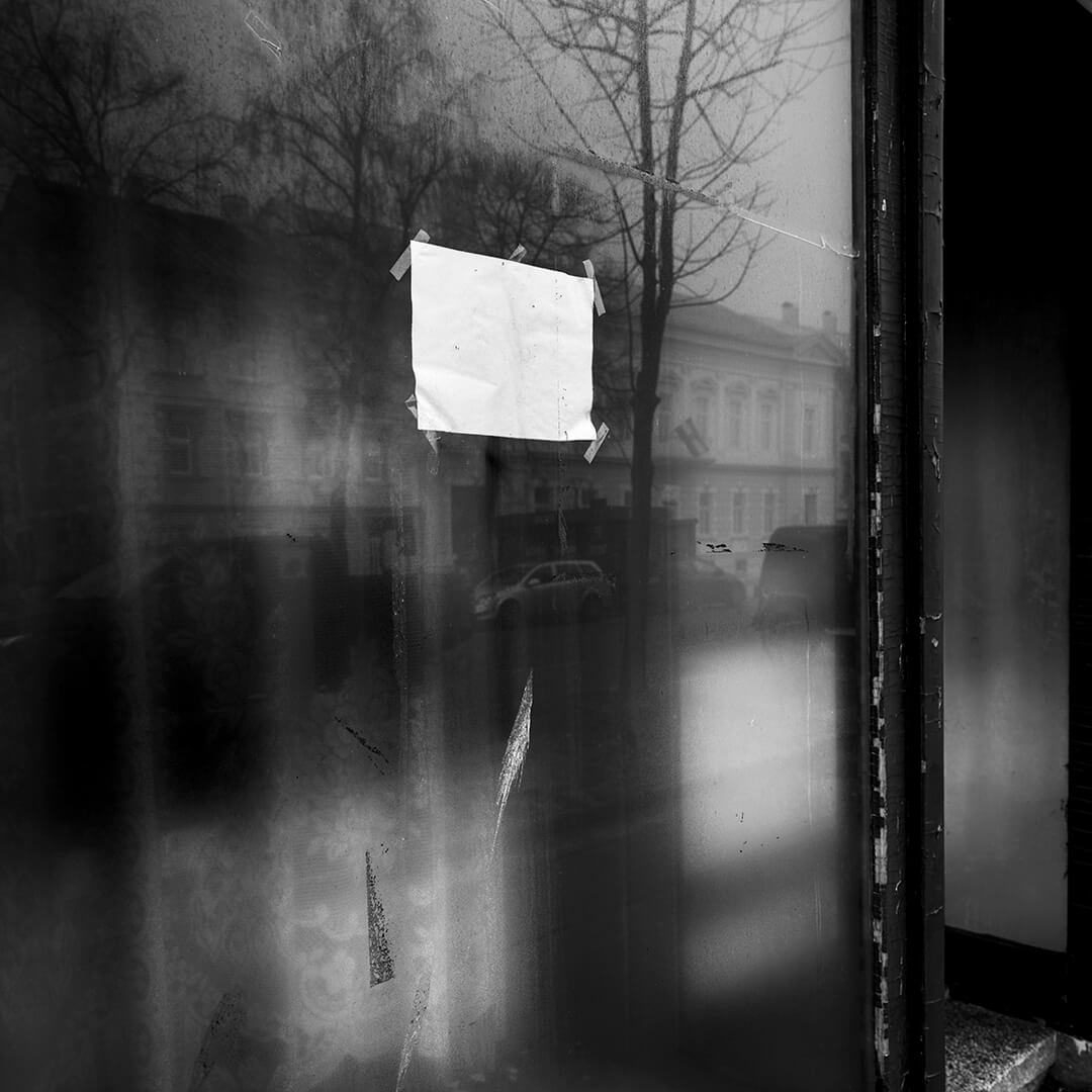 Imagem de reflexos em vidro com papéis colados no centro; ao fundo, vislumbres de edifícios e árvores.