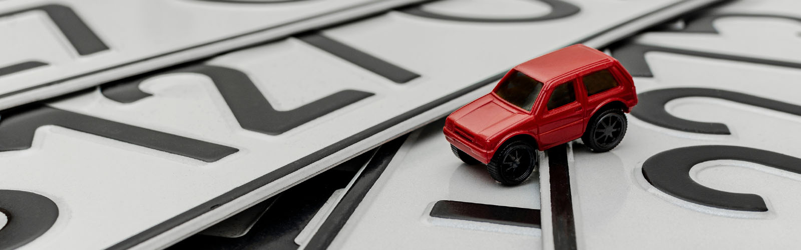 Carro encarnado sobrepoem-se  à imagem de matriculas figurando a possibilidade de verificar o seguro